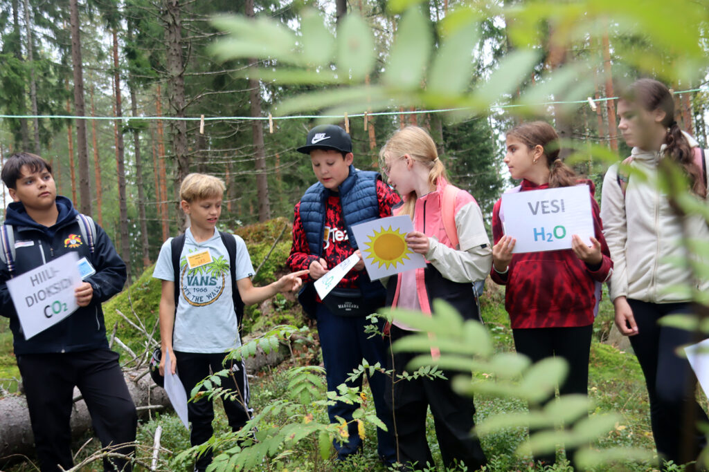 Koululaiset pohtivat yhteyttämisen kaavaa metsärastilla.